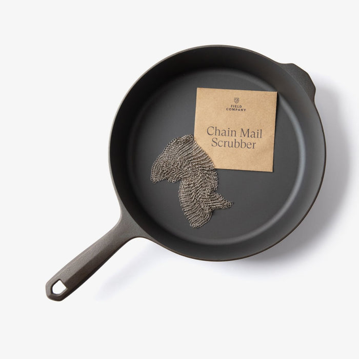 Field Company Chain Mail Scrubber and kraft packet resting inside a cast iron skillet, overhead view