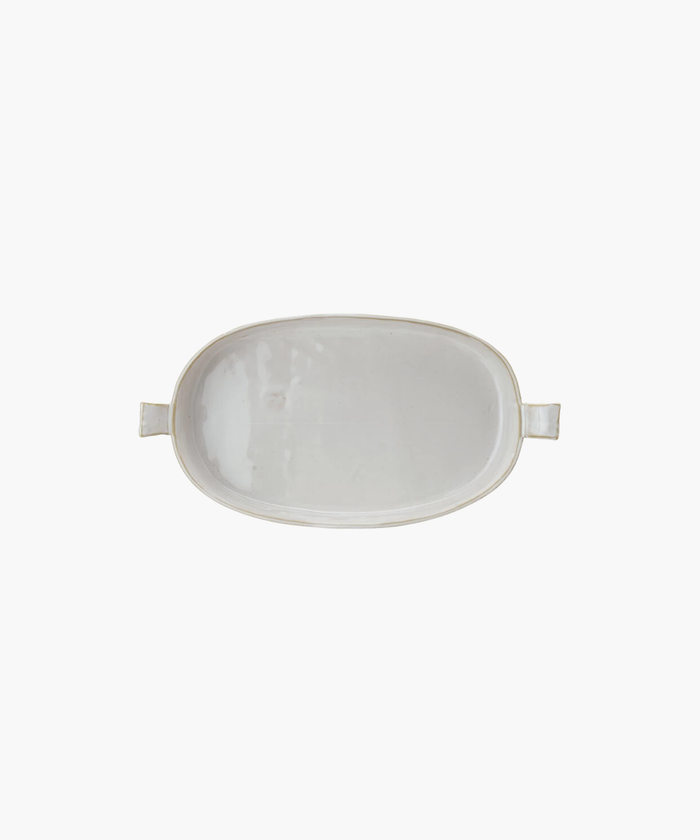 Overhead picture of an oval white ceramic stoneware baker with slightly raised, flared handles on each end. The baker has a glossy finish, conveying a minimalist, elegant design.