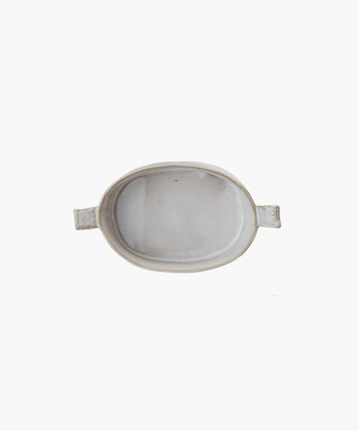 Top view of a mini oval white ceramic stoneware baker with slightly raised, flared handles on each end. The baker has a glossy finish, conveying a minimalist, elegant design.