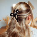 Blonde woman seen from behind wearing a black Coconut Lane bow claw clip in softly lit hair.