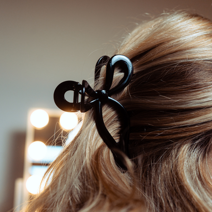Blonde hair secured with a black bow claw clip; background features softly blurred lights.