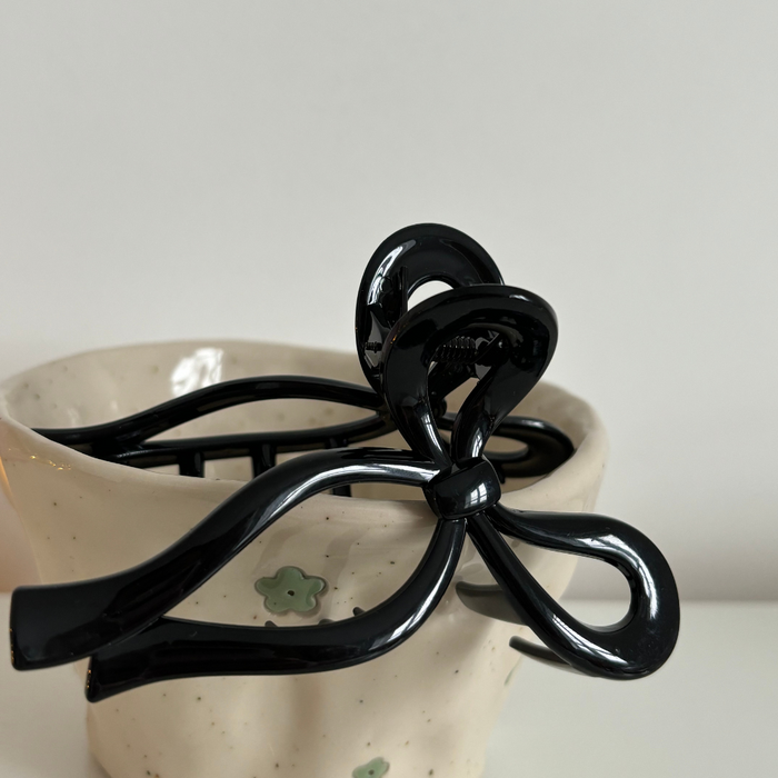Black bow claw clip from Coconut Lane clipped to a white ceramic cup with green flower designs.