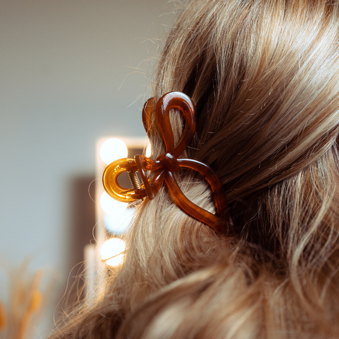 Blonde hair held by a brown bow claw clip from Coconut Lane, with soft blurred lights in the background.