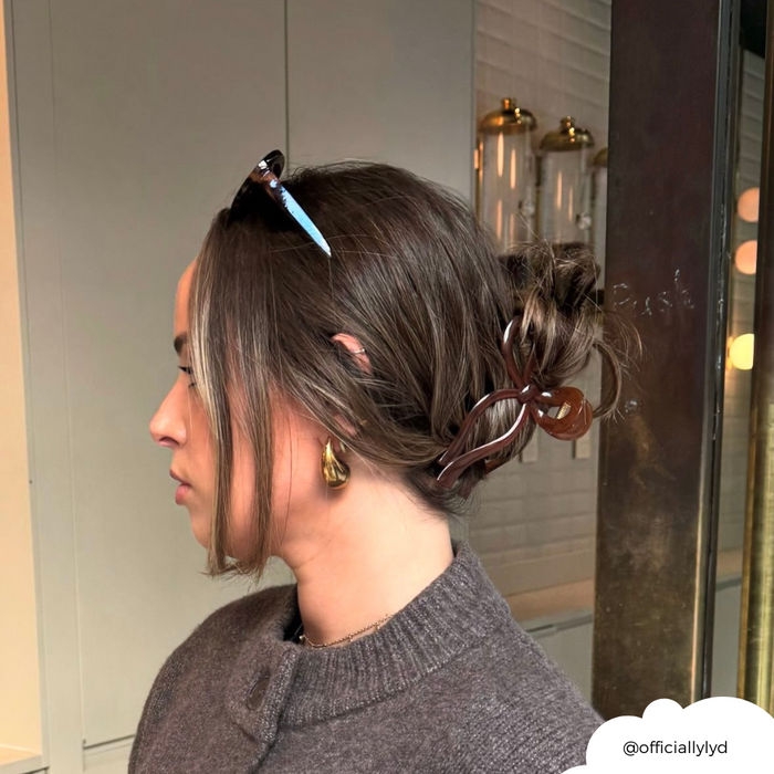 Woman with brunette hair wearing a brown Coconut Lane bow claw clip, knit sweater, gold earring, and sunglasses.
