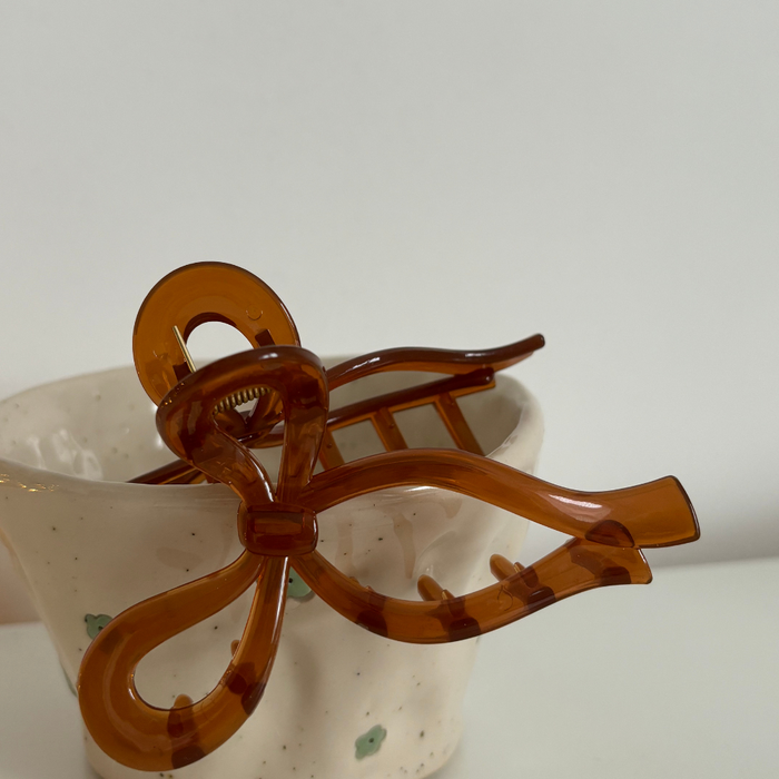 Brown bow claw clip from Coconut Lane on a white cup with green spots.