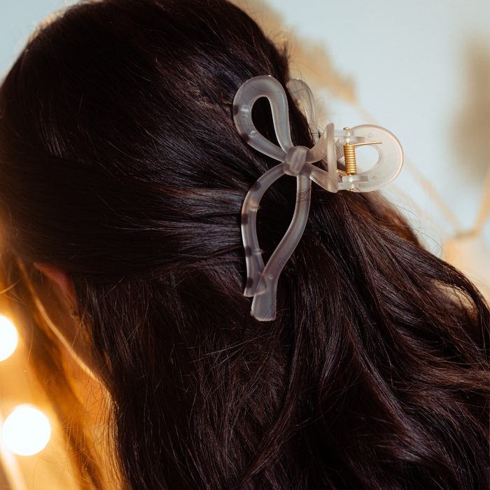 Pink bow claw clip secures brown-haired womans hair, showing off its soft fabric and playful shape.
