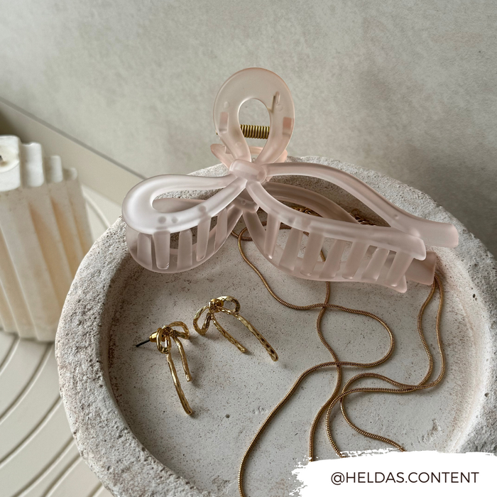 Pink bow claw clip, gold hoop earrings, and a chain necklace displayed in a textured stone dish.