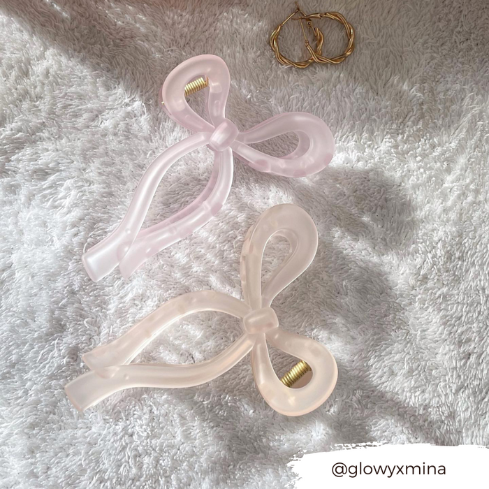 Pink bow claw clips and gold hoop earrings displayed on a soft white textured surface.