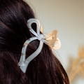 White bow claw clip from Coconut Lane securing dark hair at the back.