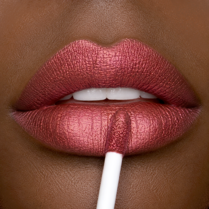 Close-up of a lip wearing Runway Rogue liquid lipstick in the shade 'Day Rate' being applied using a white applicator.