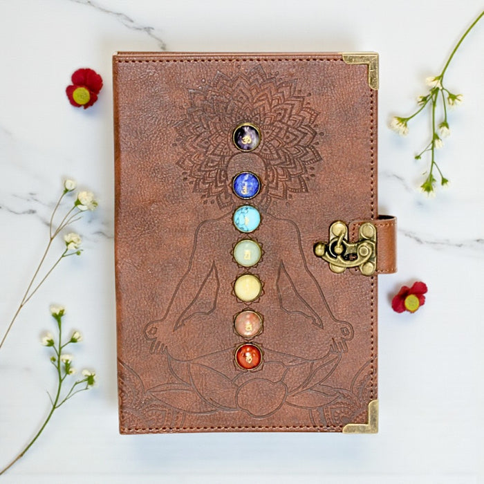 Brown leather journal with chakra design on a marble surface with flowers.