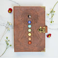 Brown leather journal with chakra design on a marble surface with flowers.