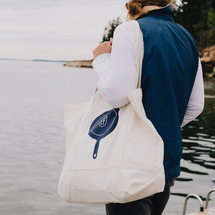 Person carrying the Field Market Tote with navy skillet graphic over one shoulder by the water