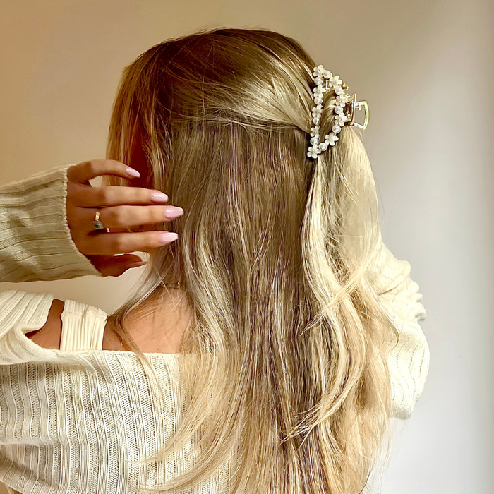 Blonde woman in a white sweater wears a Coconut Lane claw clip with floral and pearl details, plus a simple ring.