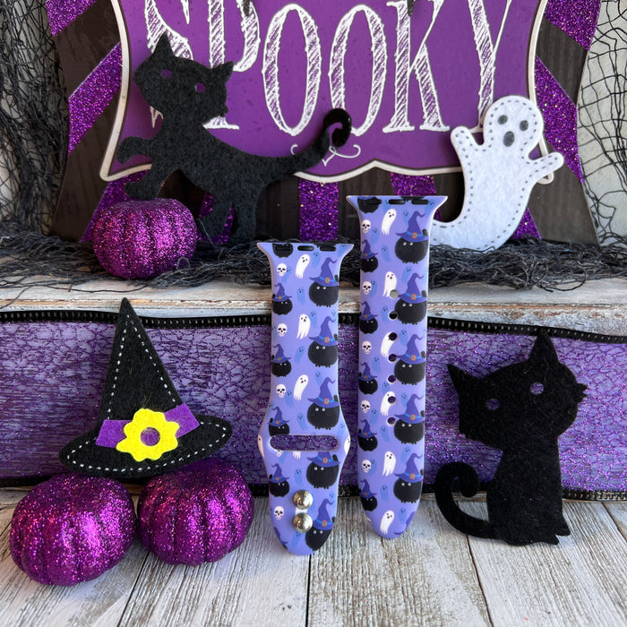 Both halves of the Ghostly Whisker's Apple Watch band standing upright against a purple SPOOKY sign with glitter pumpkins and a felt black cat.