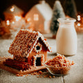 Gingerbread house with cinnamon sticks and a jar of milk on a wooden surface.