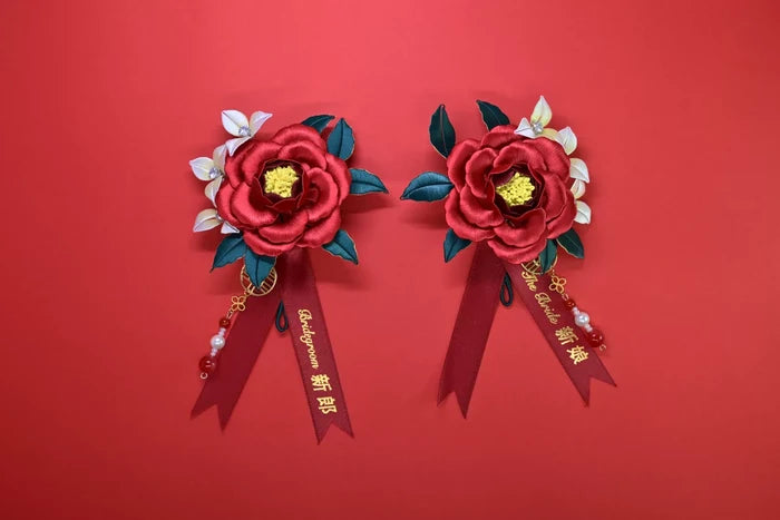 Two red handmade Chanhua bridal boutonnieres with customizable ribbons on a red background