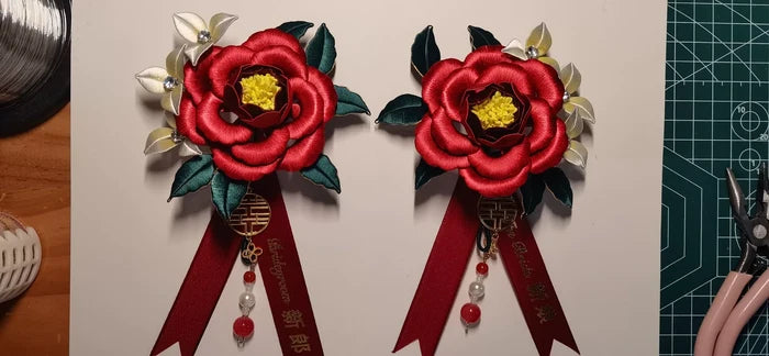 Two red handmade Chanhua bridal boutonnieres with customizable ribbons on a red background-2
