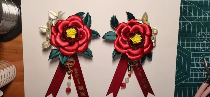 Two red handmade Chanhua bridal boutonnieres with customizable ribbons on a red background-3