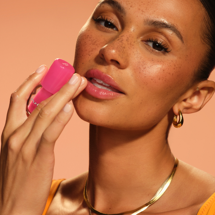 Woman applying pink lipstick against a warm-toned background