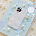 An iridescent iPhone with a Coconut Lane Mother of Pearl Phone Case is displayed on a light blue sparkly board. The background is adorned with various sizes of pearls and holographic circles, creating a whimsical and elegant arrangement.