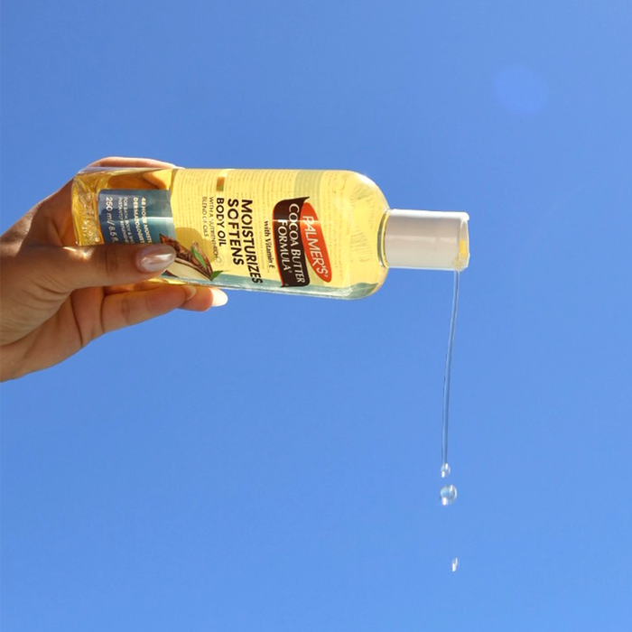 Hand holding a bottle of Palmer's Cocoa Butter Formula body oil against a blue sky.