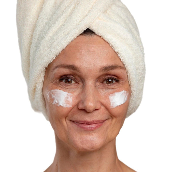 White woman in white head towel with face cream  on cheeks. Best anti-aging cream for face. Dermal Essentials Medical Grade Skincare.