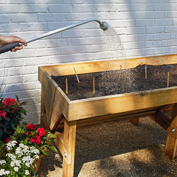 Raised wooden planter bed with seed stakes, watered from a hose