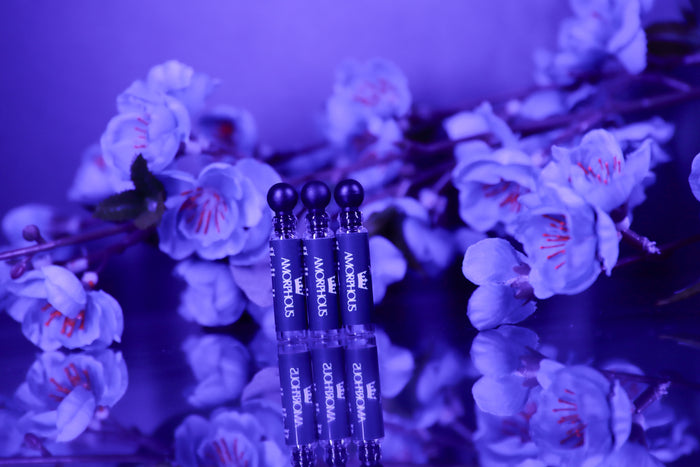 Three perfume samples with labels on a reflective surface with flowers in the background