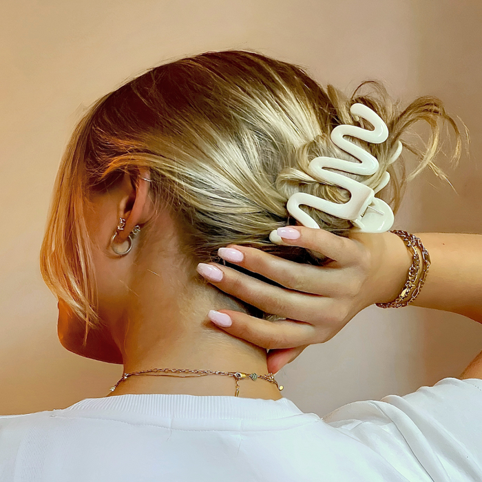 Blonde hair twisted and secured with a cream squiggle claw clip; manicured nails and gold jewelry visible.