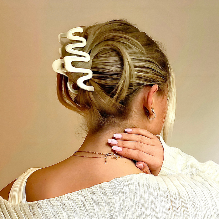 Woman with blonde hair in an updo, wearing a cream Coconut Lane squiggle claw clip and a white top.