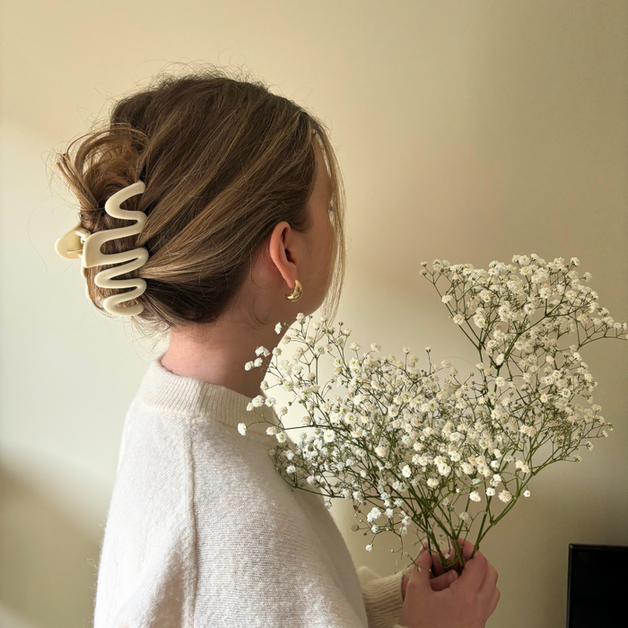Woman facing away with a cream squiggle claw clip in her hair, holding babys breath against a beige wall.