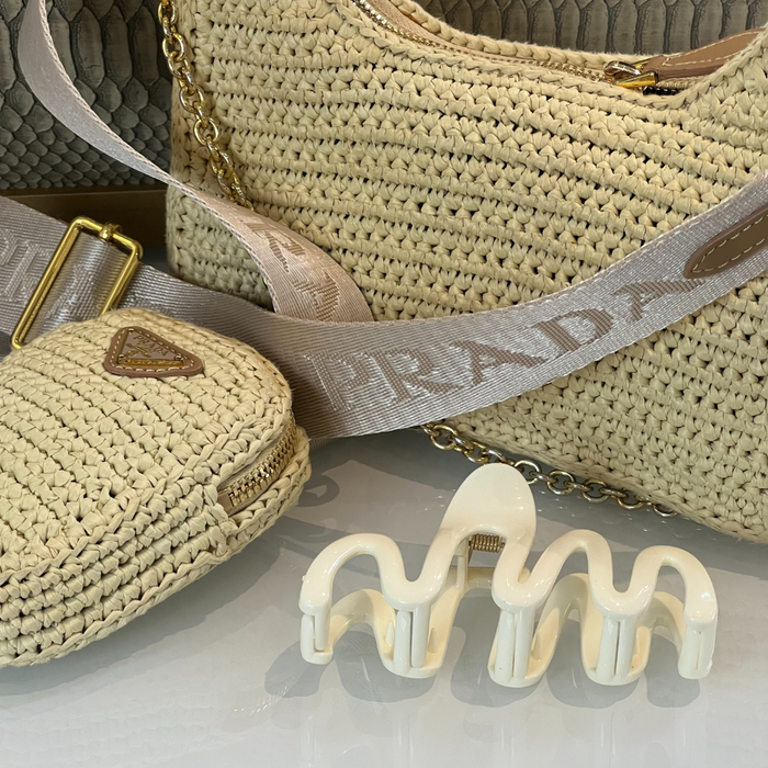 Beige woven Prada handbags and coin purse with cream squiggle claw clip, displayed on a reflective surface.