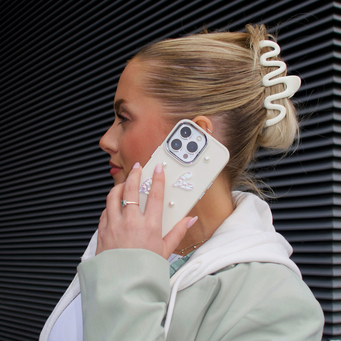 Cream Squiggle Claw Clip by Coconut Lane securing womans hair; she wears a light green jacket and white hoodie, holding a phone.