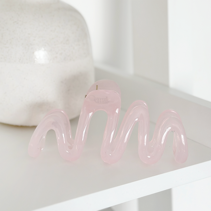 Pink squiggle claw clip by Coconut Lane on a white shelf beside a textured white ceramic vase.