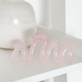 Pink squiggle claw clip by Coconut Lane on a white shelf beside a textured white ceramic vase.