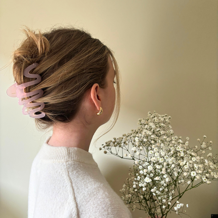 Woman with hair in a pink Coconut Lane Squiggle Claw Clip holds babys breath, facing away by a beige wall.