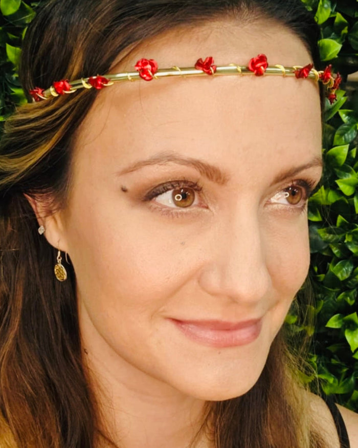 Model wearing a gold floral crown headband with small red rose accents for festival or wedding wear.