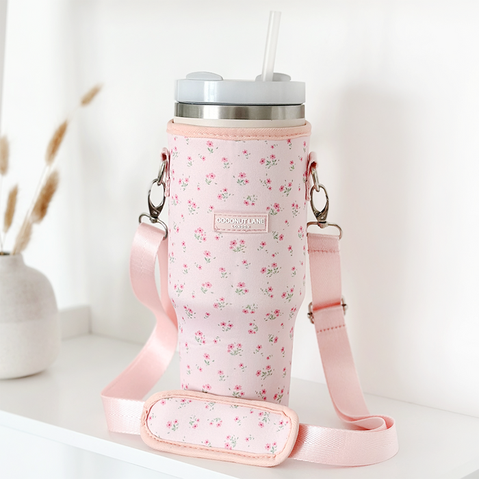 Pink tumbler carry case with ditsy floral pattern and strap displayed on a shelf.