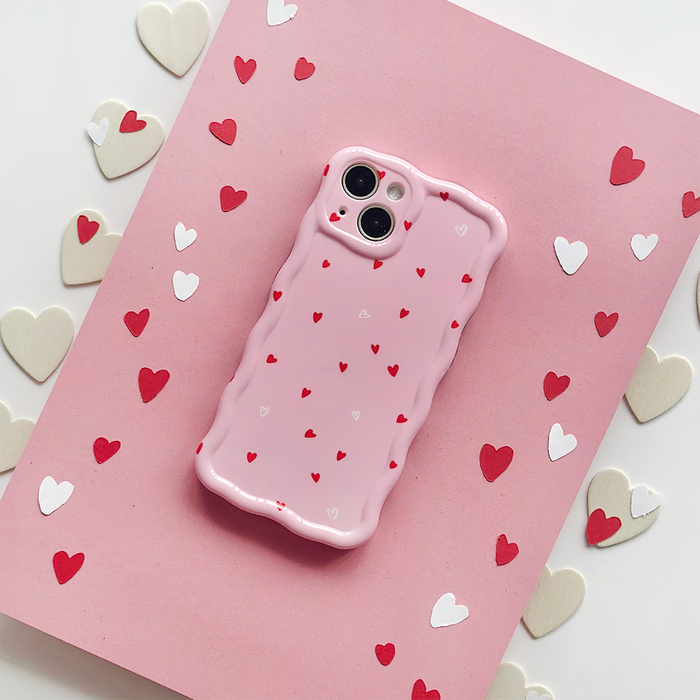 Pink wavy phone case with red and white hearts, shown on a pink background with paper heart decorations.