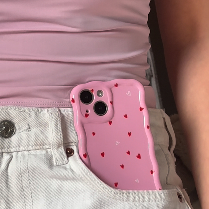 Pink heart-patterned wavy phone case partially tucked in white jeans, next to a pink shirt.