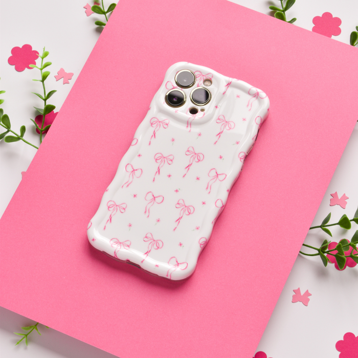White wavy phone case with pink sections and small bow pattern, accented by flowers and green leaves.