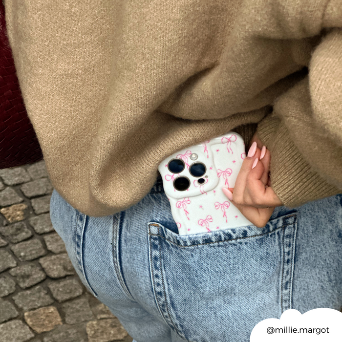 A wavy phone case with dainty bow pattern is slipped into the pocket of light blue jeans, paired with a beige sweater.