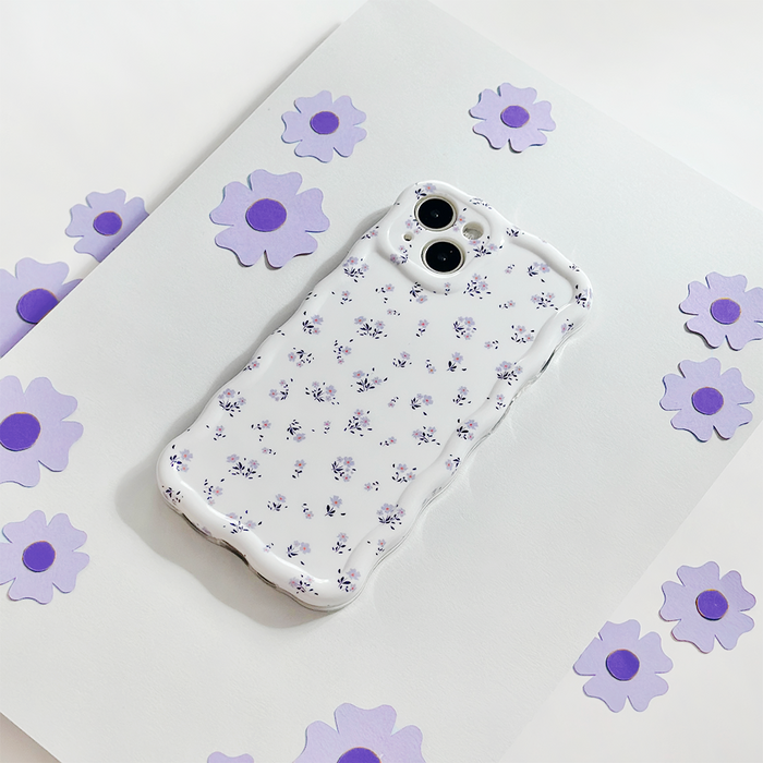 Coconut Lane wavy phone case with ditsy floral pattern in periwinkle, displayed on paper with purple flower cutouts.