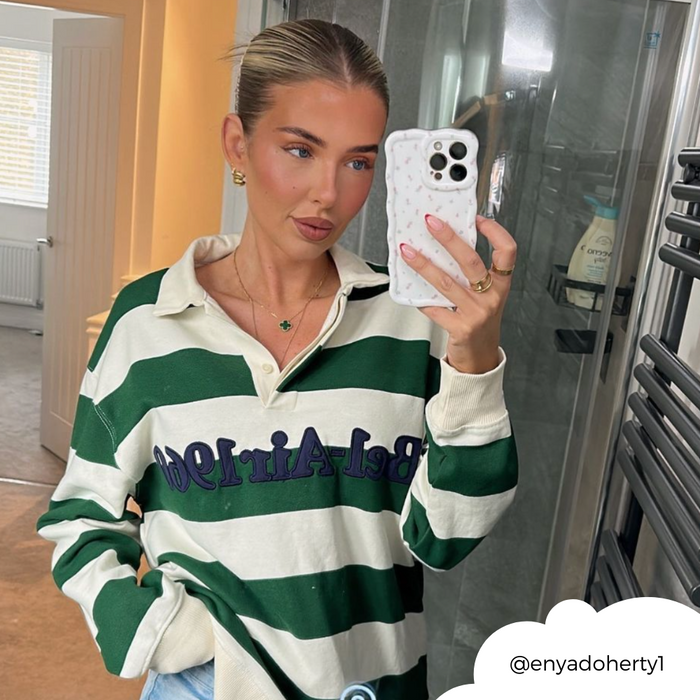 Woman in a green striped shirt takes a mirror selfie holding a white phone case with a ditsy floral wavy design.