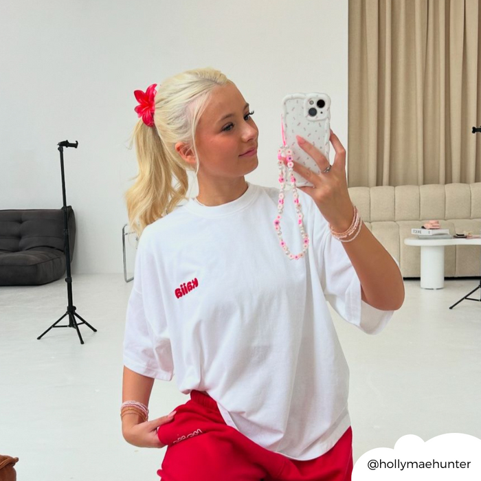 Blonde woman in white tee and red pants holds a phone with a Coconut Lane case featuring a wavy ditsy floral pattern.