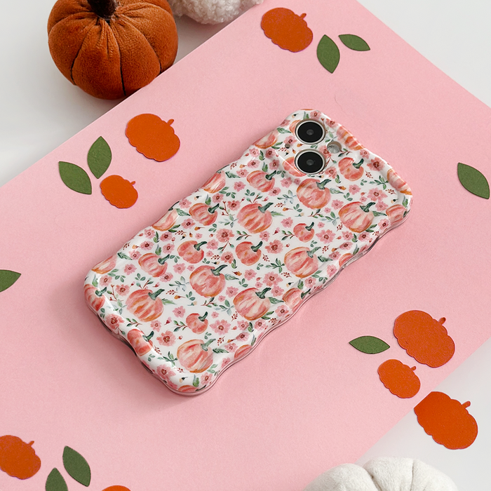 Phone with Coconut Lane wavy case featuring a ditsy pumpkin pattern, shown on a pink surface with paper pumpkins.