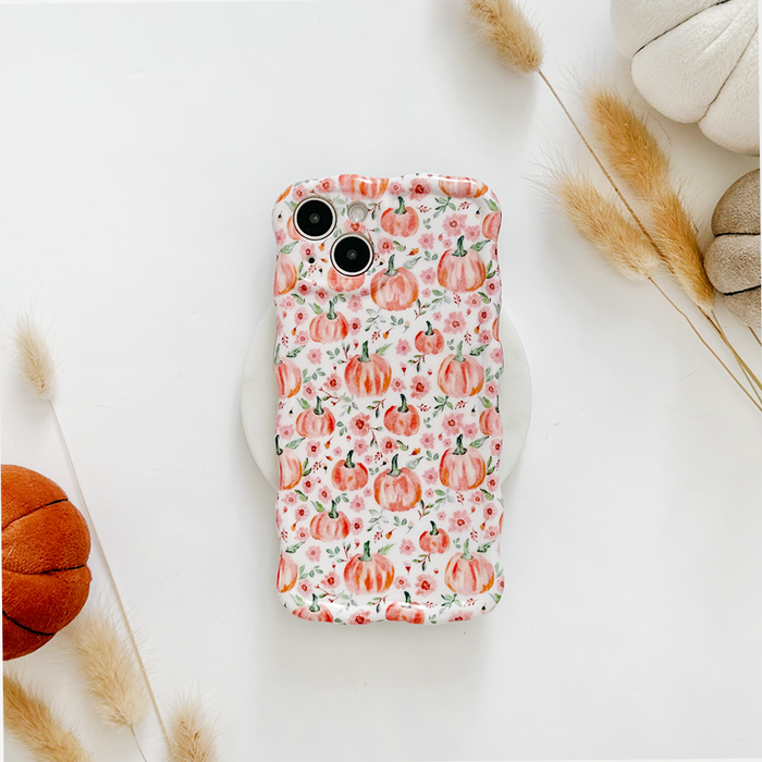 Coconut Lane wavy phone case with a ditsy pumpkin pattern on a white surface, surrounded by fall decor and dried grasses.