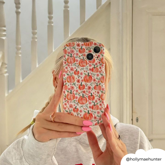 Hand with pink nails holds a wavy phone case with a ditsy pumpkin pattern, shown in a mirror near white stairs.