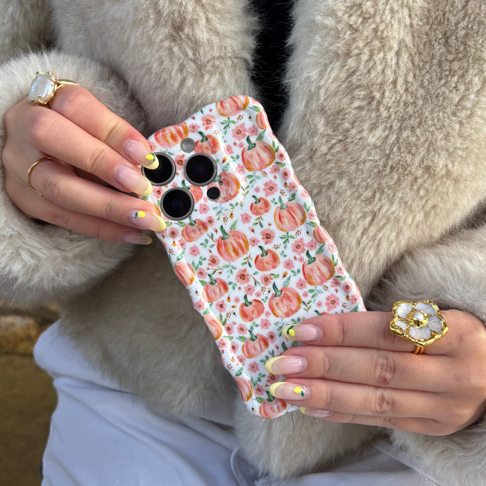 Coconut Lane Wavy Phone Case in Ditsy Pumpkins pattern, held by hands with gold rings and yellow-tipped nails.